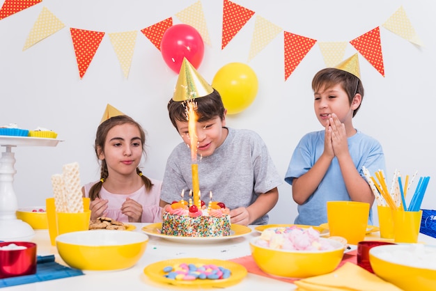 Foto gratuita amigos aplaudiendo mientras chico cortando su pastel de cumpleaños en casa