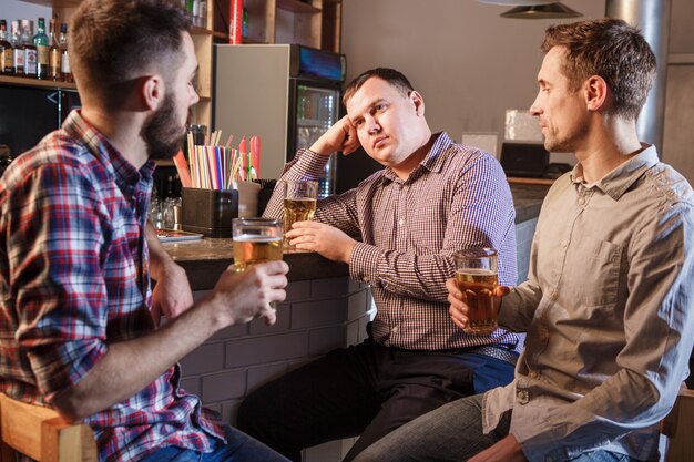 Los amigos bebiendo cerveza en el mostrador en pub