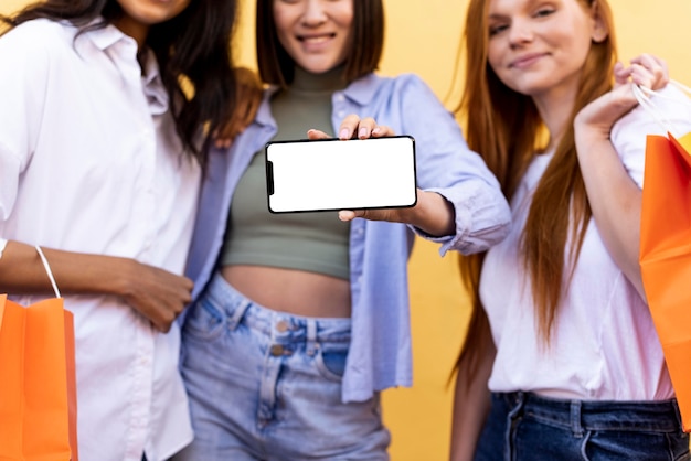 Amigos con bolsas de la compra y un teléfono en blanco