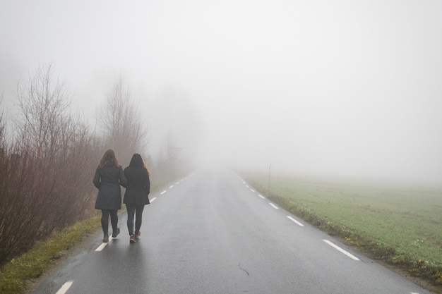 Amigos caminando por una carretera que conduce a la niebla