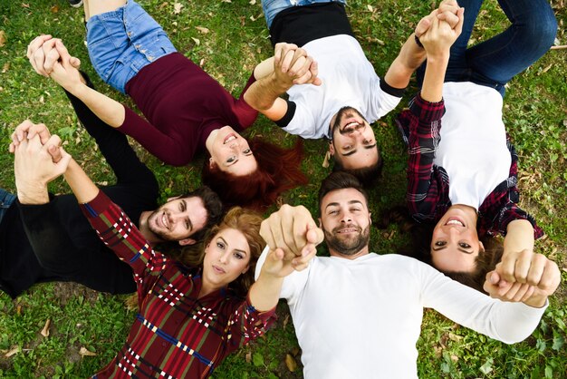 Amigos cogidos de las manos tumbados en el césped de un parque