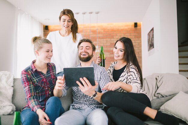 Amigos contentos que se enfrían con la tableta en el sofá