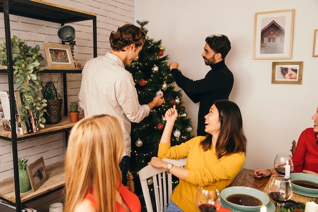 Amigos decorando árbol en cena de navidad