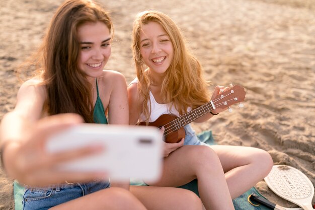 Amigos disfrutando de tocar el ukelele tomando selfie en la playa