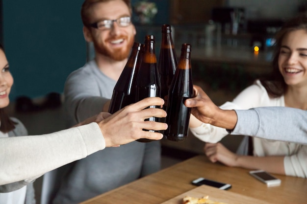 Amigos diversos tintinean botellas de cerveza artesanal en pub, concepto de salud