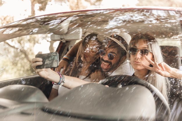 Amigos divertidos tomando selfie dentro del coche en el teléfono móvil