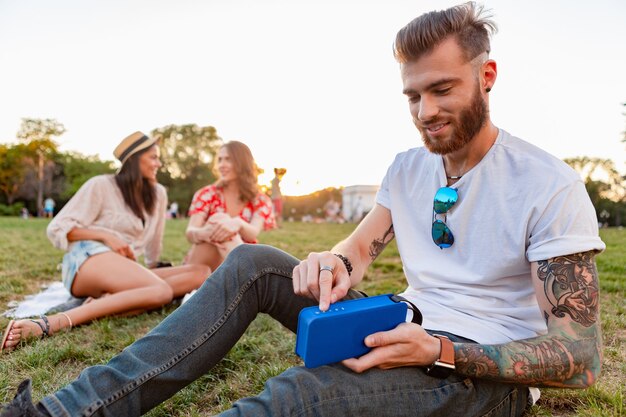 Amigos divirtiéndose juntos en el parque sonriendo escuchando música en el altavoz inalámbrico