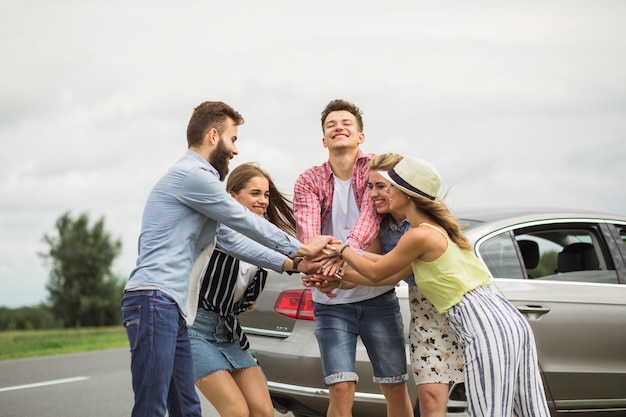 Amigos felices apilando la mano de cada uno de pie cerca del coche