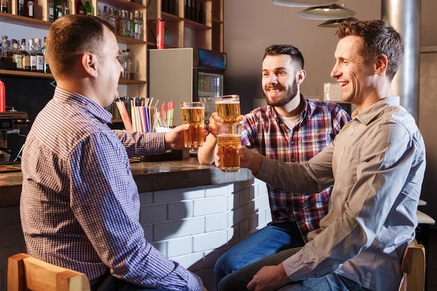 Amigos felices bebiendo cerveza en el mostrador en pub