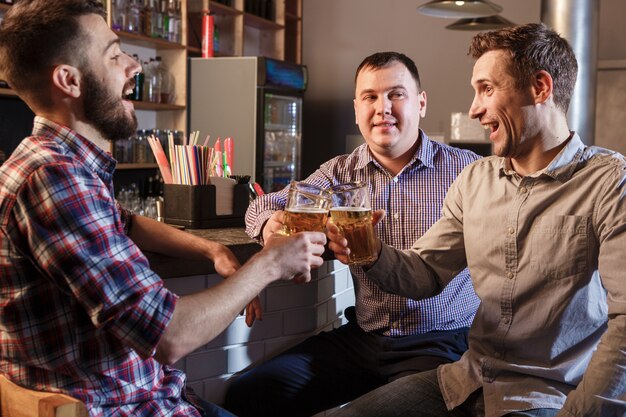 Amigos felices bebiendo cerveza en el mostrador en pub