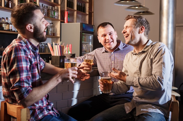 Amigos felices bebiendo cerveza en el mostrador en pub