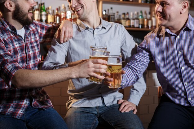 Amigos felices bebiendo cerveza en el mostrador en pub