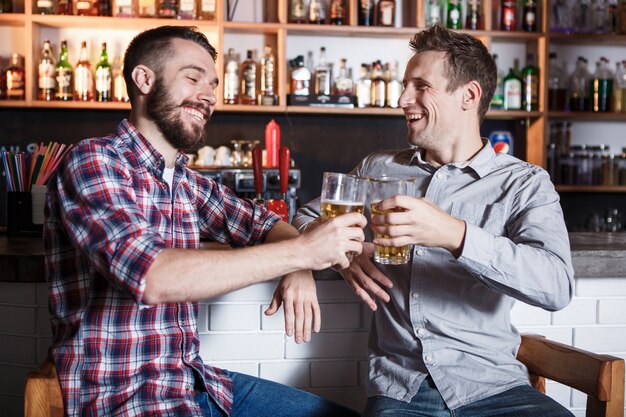 Amigos felices bebiendo cerveza en el mostrador en pub