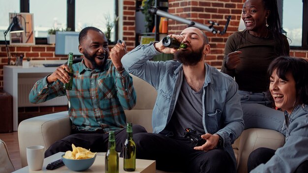 Amigos felices celebrando la victoria de los videojuegos en la consola de televisión, jugando y ganando en la reunión con cerveza. La gente se siente alegre por la competencia de juegos en línea, la actividad de ocio.