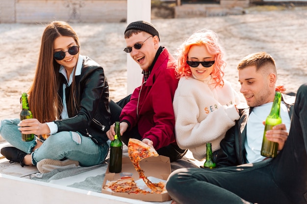 Amigos felices con cerveza y pizza en picnic