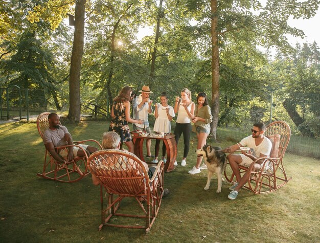 Amigos felices comiendo y bebiendo cervezas en la cena de barbacoa al atardecer