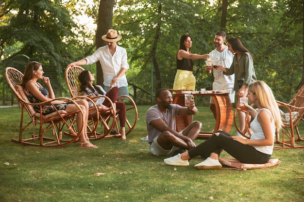 Amigos felices comiendo y bebiendo cervezas en la cena de barbacoa al atardecer