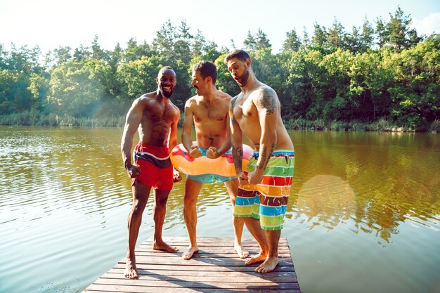 Amigos felices divirtiéndose, listos para saltar y nadar en el río