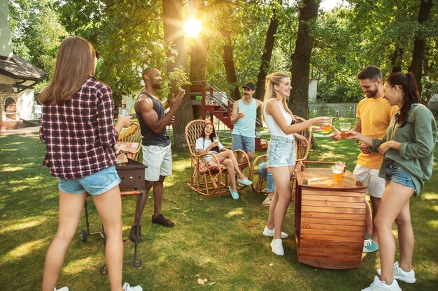 Amigos felices están tomando cerveza y fiesta de barbacoa en un día soleado