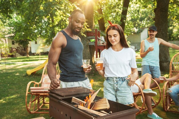 Amigos felices están tomando cerveza y fiesta de barbacoa en un día soleado