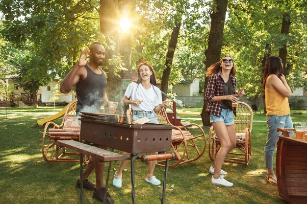 Amigos felices están tomando cerveza y fiesta de barbacoa en un día soleado