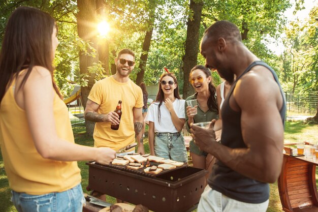 Amigos felices están tomando cerveza y fiesta de barbacoa en un día soleado