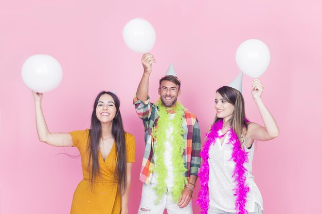 Amigos felices con globos blancos sobre fondo rosa