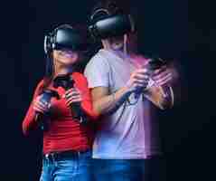 Foto gratuita amigos felices jugando videojuegos con gafas de realidad virtual con controladores. aislado sobre fondo oscuro. foto con efecto de luz.