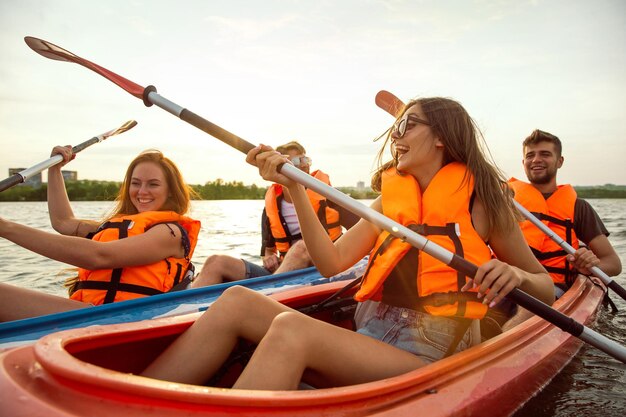Amigos felices en kayak en el río con puesta de sol en el fondo