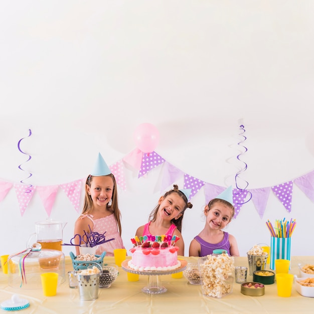 Amigos felices que disfrutan de la fiesta de cumpleaños con sabroso bocadillo y pastel en la mesa