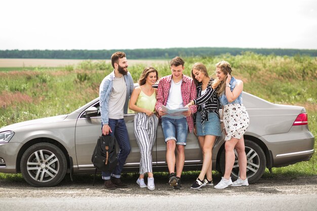 Amigos felices que miran el mapa que se coloca cerca del coche