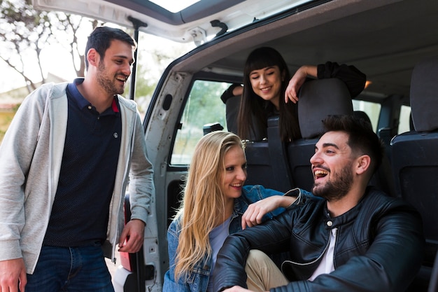 Amigos felices que se sientan en el tronco del coche