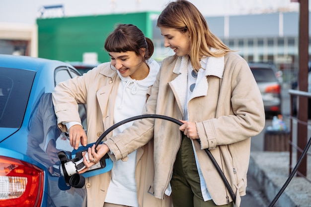 Amigos felices repostar el coche en la gasolinera. Viaje de vacaciones de amigos