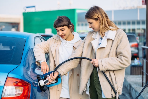 Amigos felices repostar el coche en la gasolinera.