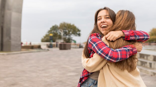 Amigos felices de tiro medio abrazándose afuera