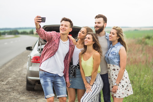 Amigos felices en viaje por carretera tomando selfie en smartphone