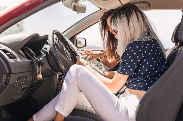 Amigos femeninos modernos que se sientan en el coche que busca destinos en el mapa
