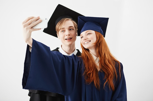 Amigos graduados de la universidad en mayúsculas sonriendo haciendo selfie.