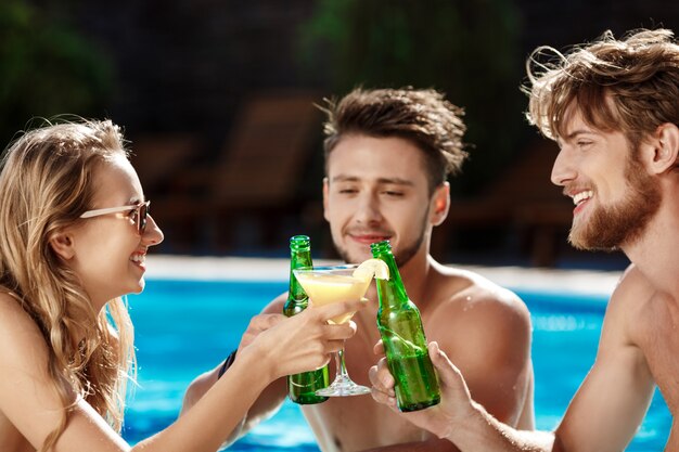 Amigos hablando, sonriendo, bebiendo cócteles, descansando, relajándose cerca de la piscina