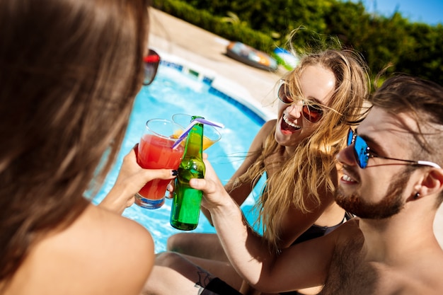 Amigos hablando, sonriendo, bebiendo cócteles, descansando, relajándose cerca de la piscina