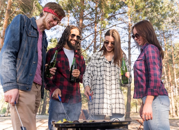 Foto gratuita amigos haciendo una barbacoa al aire libre mientras beben cervezas