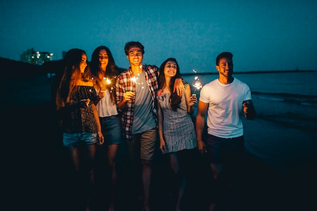 Amigos jóvenes con bengalas en una playa de noche