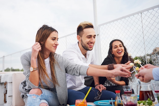 Amigos jóvenes felices estaban sentados en una mesa y haciendo un picnic al aire libre.