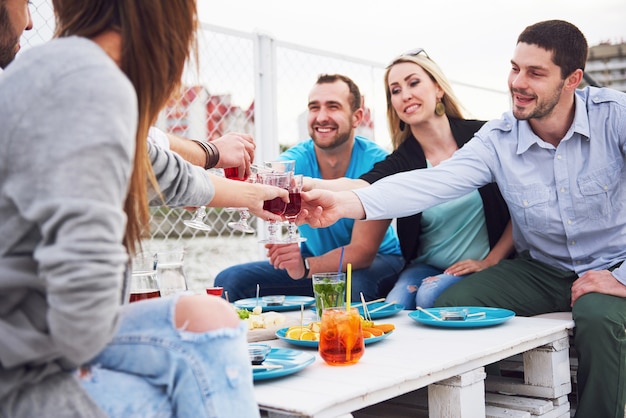 Amigos jóvenes felices estaban sentados en una mesa y haciendo un picnic al aire libre.