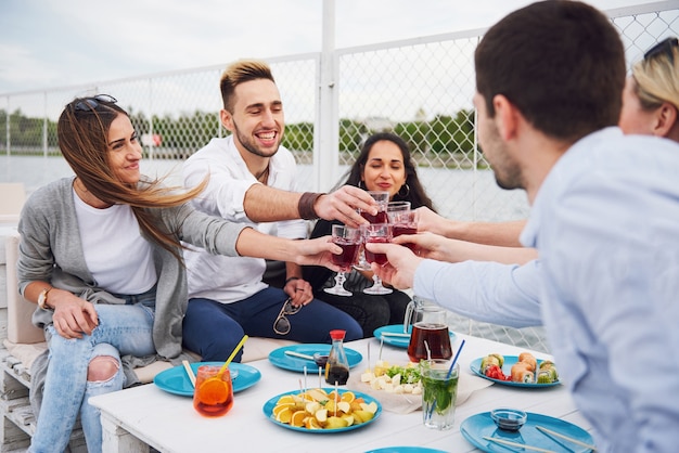 Amigos jóvenes felices estaban sentados en una mesa y haciendo un picnic al aire libre.