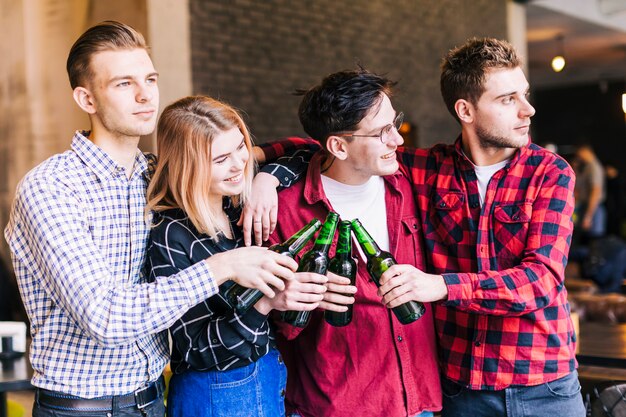 Amigos jóvenes tintineando con botellas de cerveza en el bar