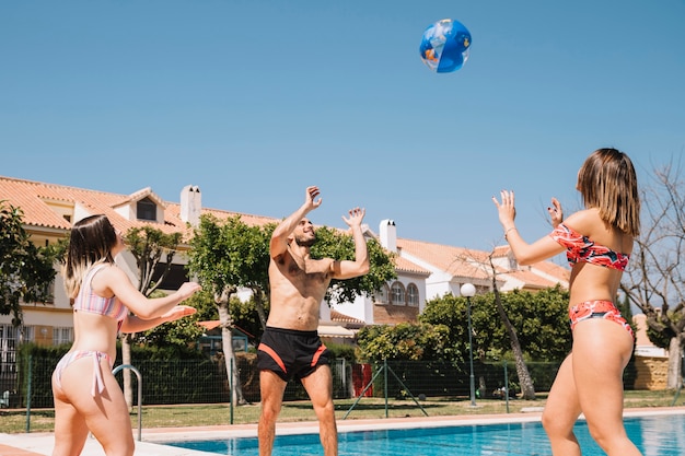 Amigos jugando con pelota al lado de piscina