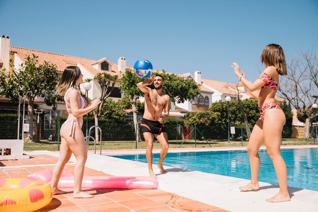 Amigos jugando con pelota al lado de piscina