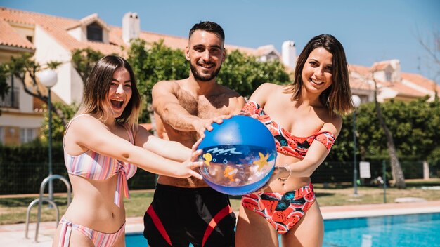 Amigos jugando con pelota al lado de piscina