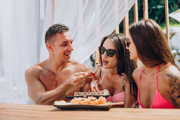 Amigos juntos comiendo rollos de sushi en la piscina